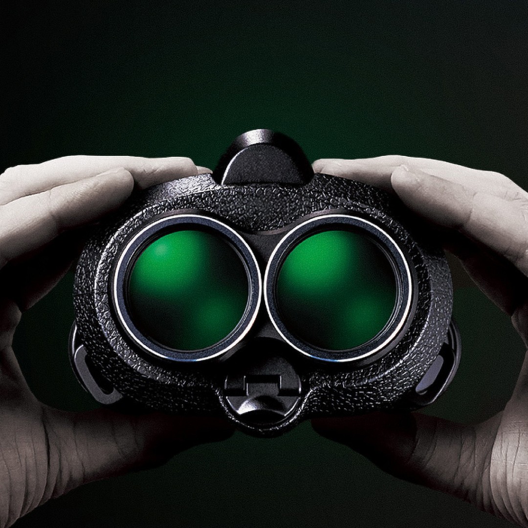 Two hands holding a pair of binoculars face on against a dark green glow: two round lenses side by side, joined in the middle.
