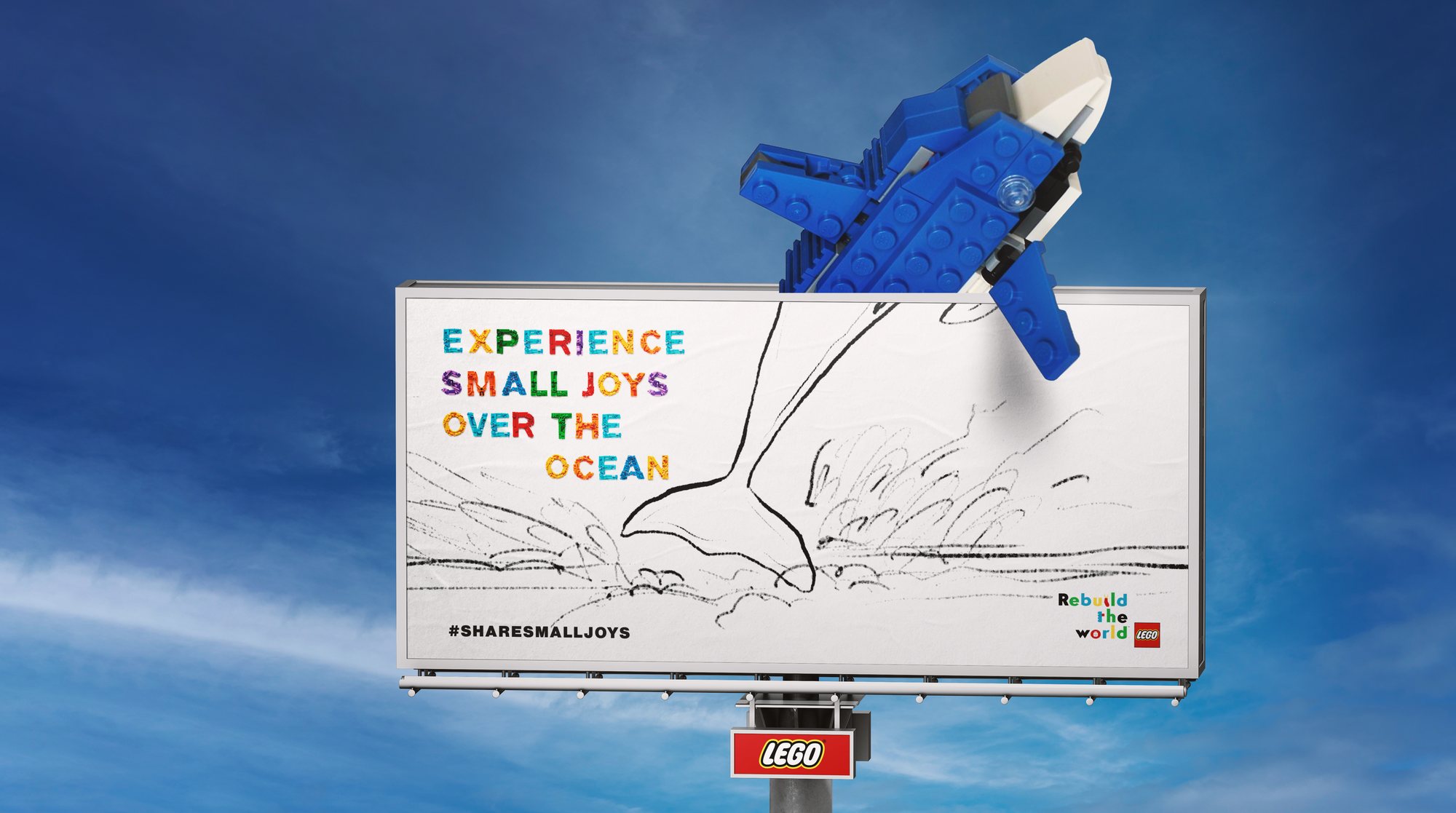 A billboard against a blue sky with a pencil drawing of a splashing sea. A dolphin built from blue and white LEGO bricks leaps out over the top of the board. The headline reads Experience small joys over the ocean.