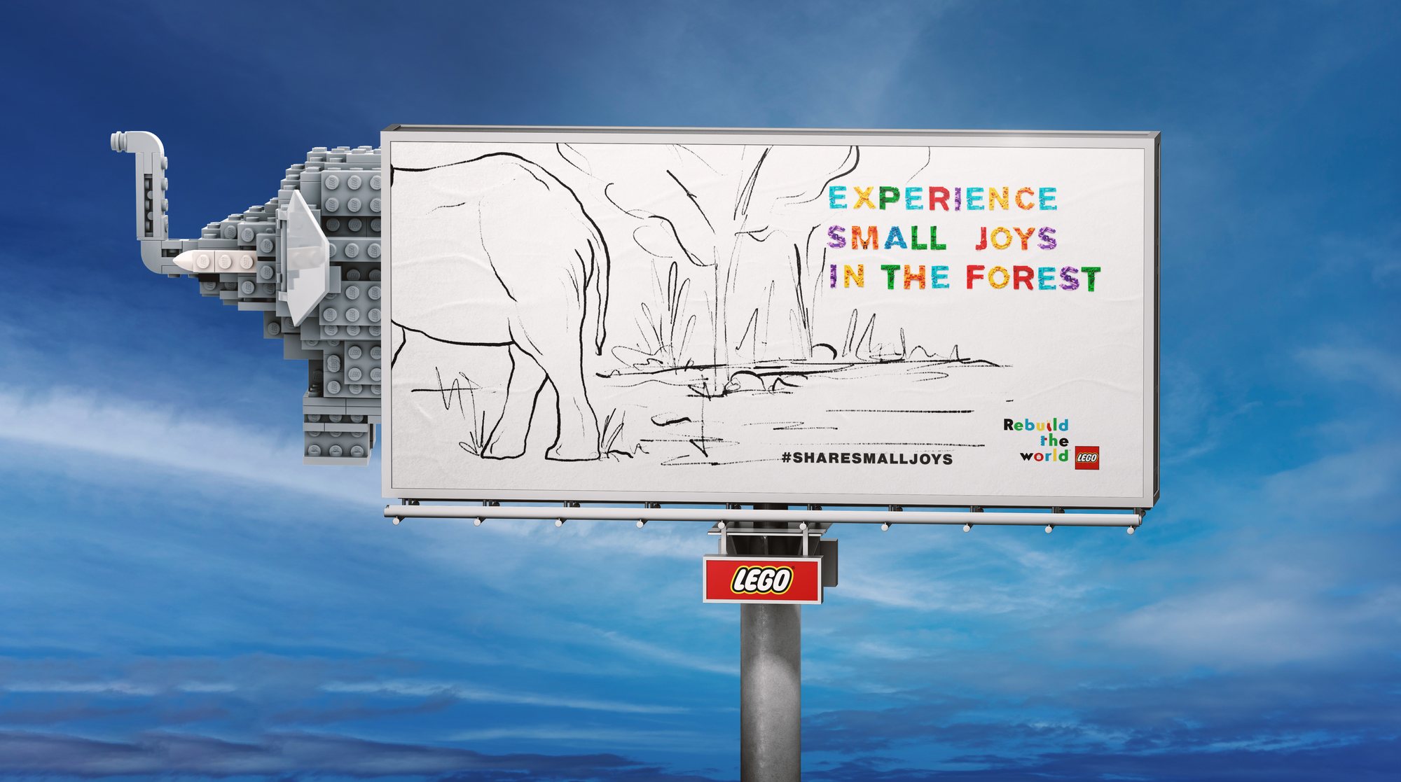 A billboard against a blue sky with a pencil drawing of an elephant by a river. The elephant's head, built from gray LEGO bricks, sticks out past the left edge of the board. The headline reads Experience small joys in the forest.